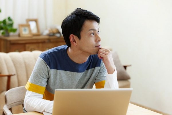 パソコンを開けて考え事をする男性
